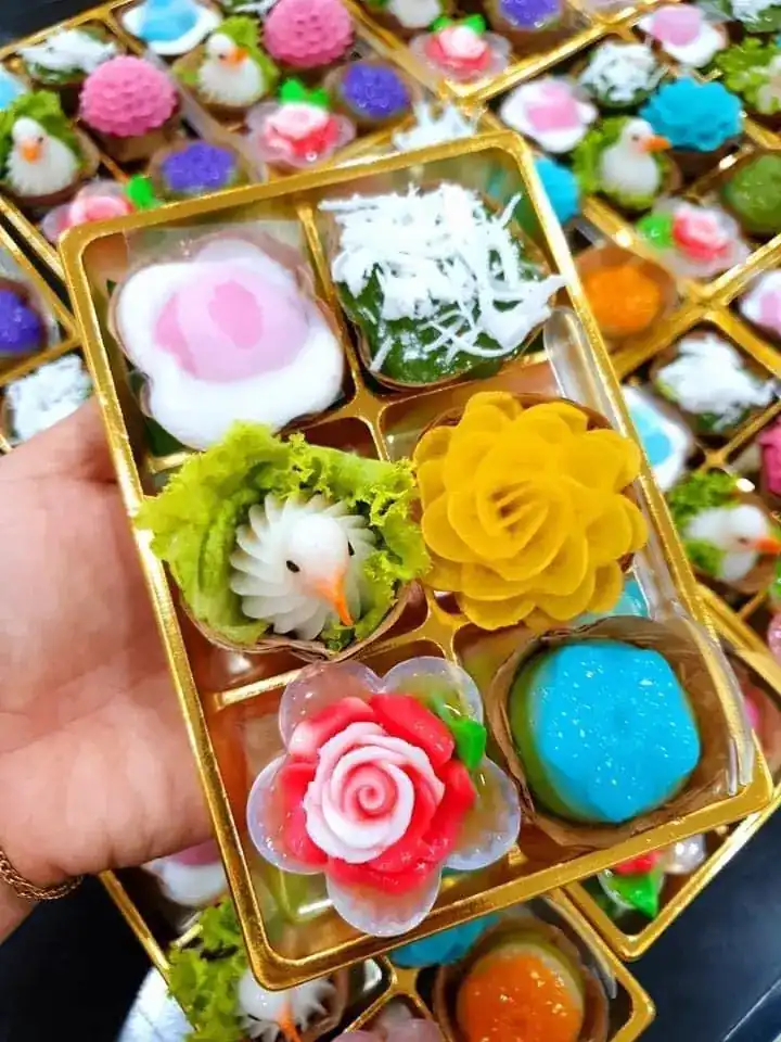 A hand holding a gold box of six assorted Thai sweets