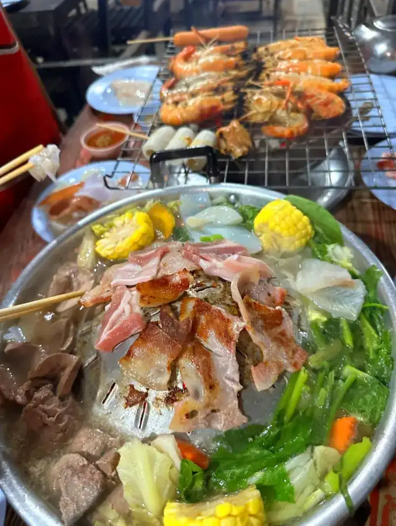 Moo kratha with pork on the dome, corn and greens in the broth, and prawns on the grill behind