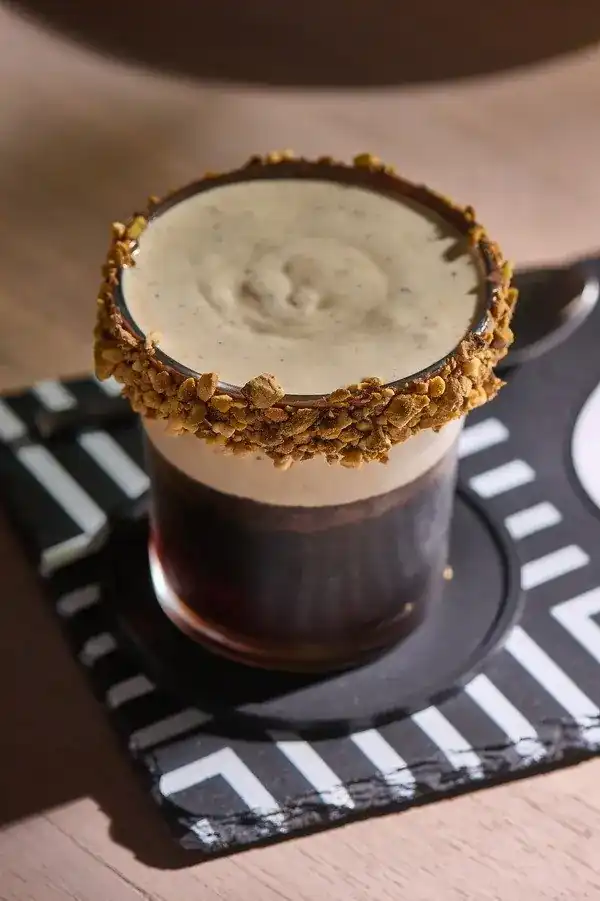 Rafiki Tachio: cold brew under pistachio cream, the rim of the glass rolled in crushed pistachio