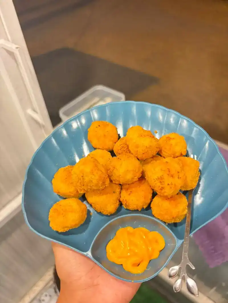 A shell-shaped plate of golden fried bites with a yellow dipping sauce, held in one hand