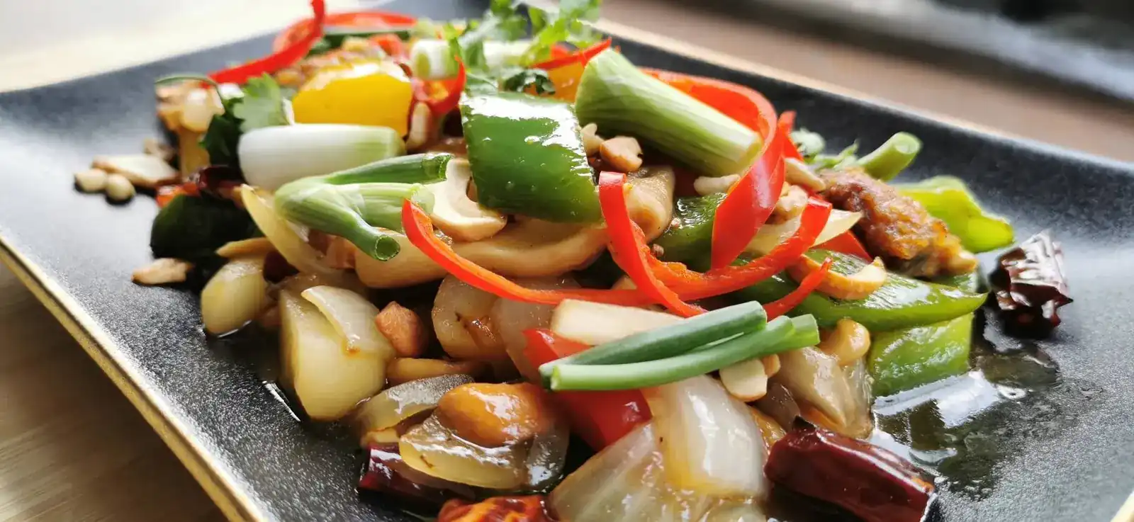 Fried Sweet N Sour Chikin Cashew Nut with peppers, onion and spring onion on a black plate