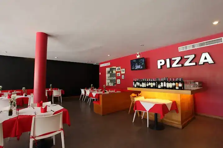 Dining room with a red wall, the word PIZZA in white letters, and tables in red and white cloths