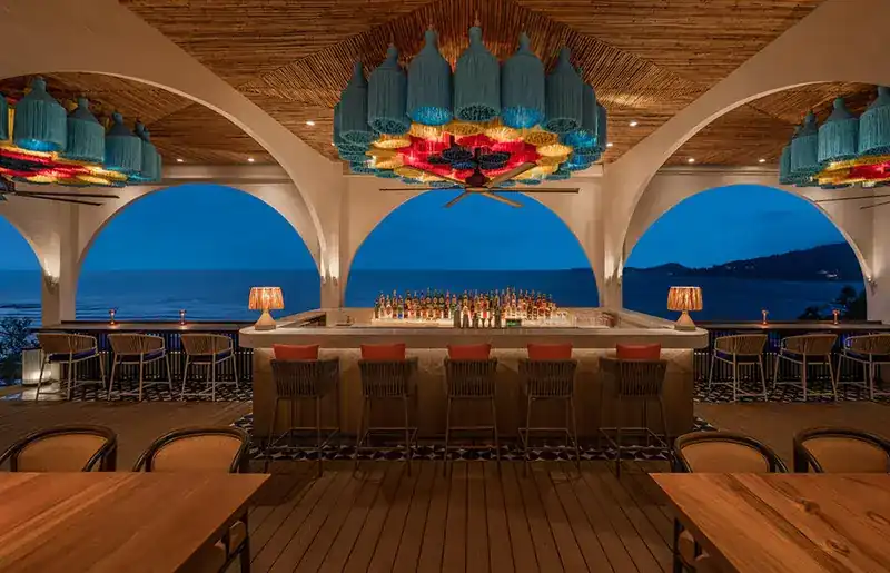 The top-floor bar at twilight, open to the sea, under tasselled blue lamps
