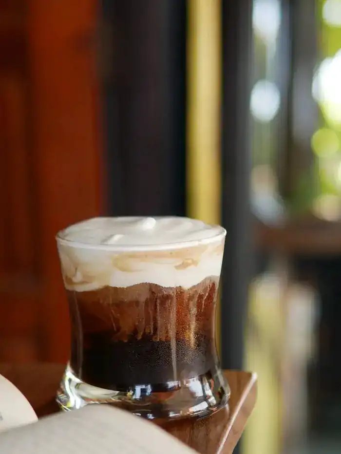 Iced specialty coffee topped with cream, on a wooden table at MMA GUY Cafe