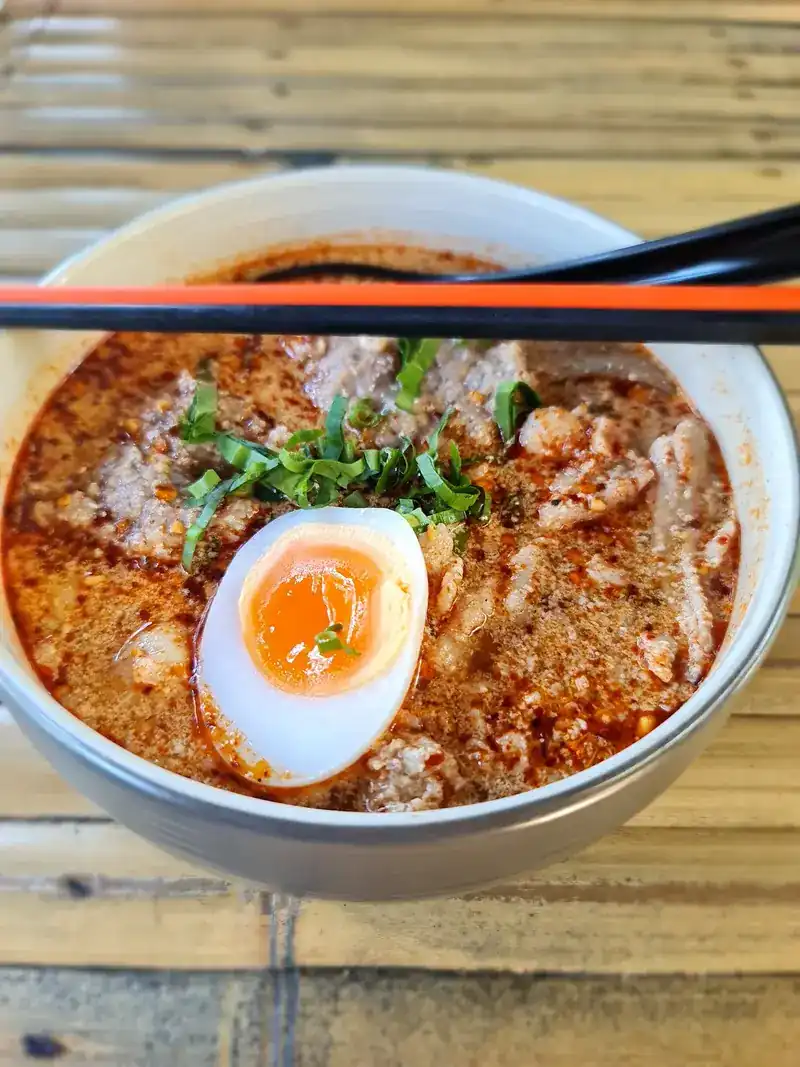 Bowl of thick tom yum with pork and a soft-boiled egg, seen from above