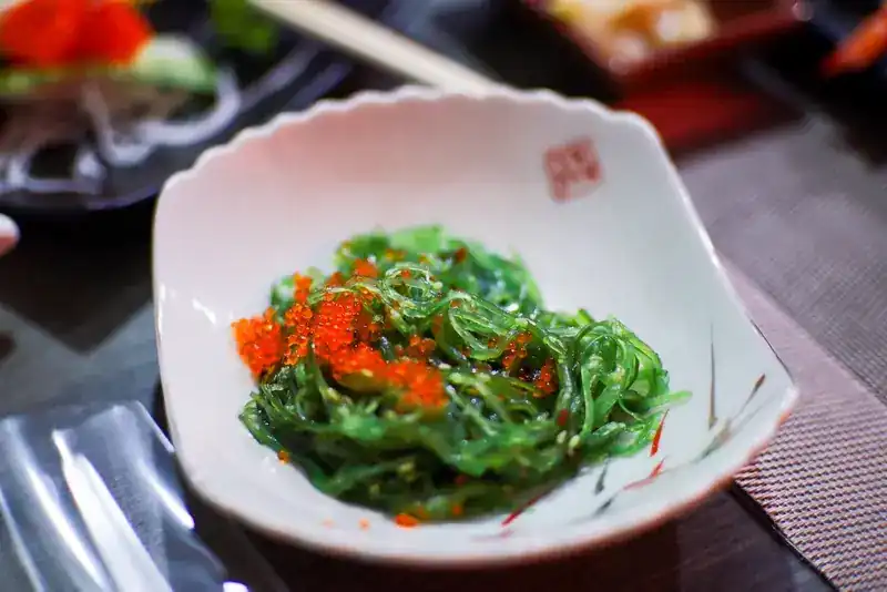 Green seaweed salad topped with orange fish roe in a white bowl