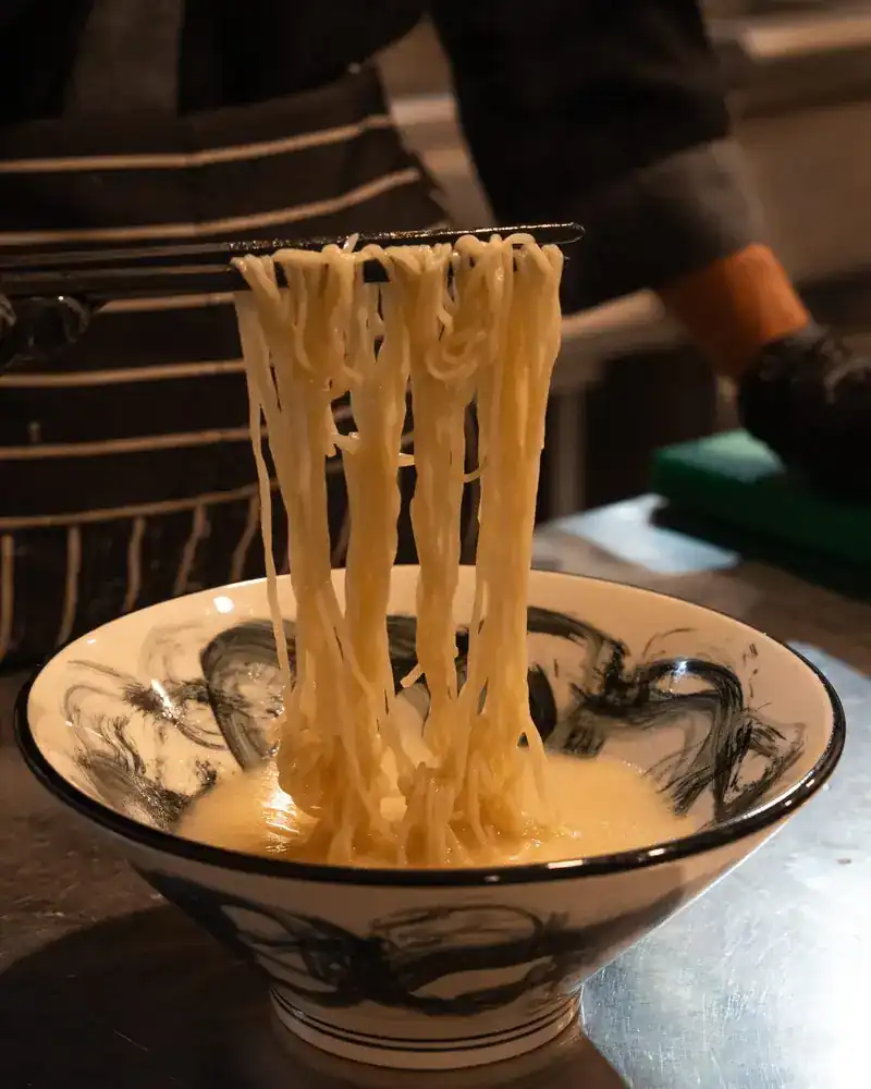 Fresh noodles lifted with chopsticks from a bowl of broth