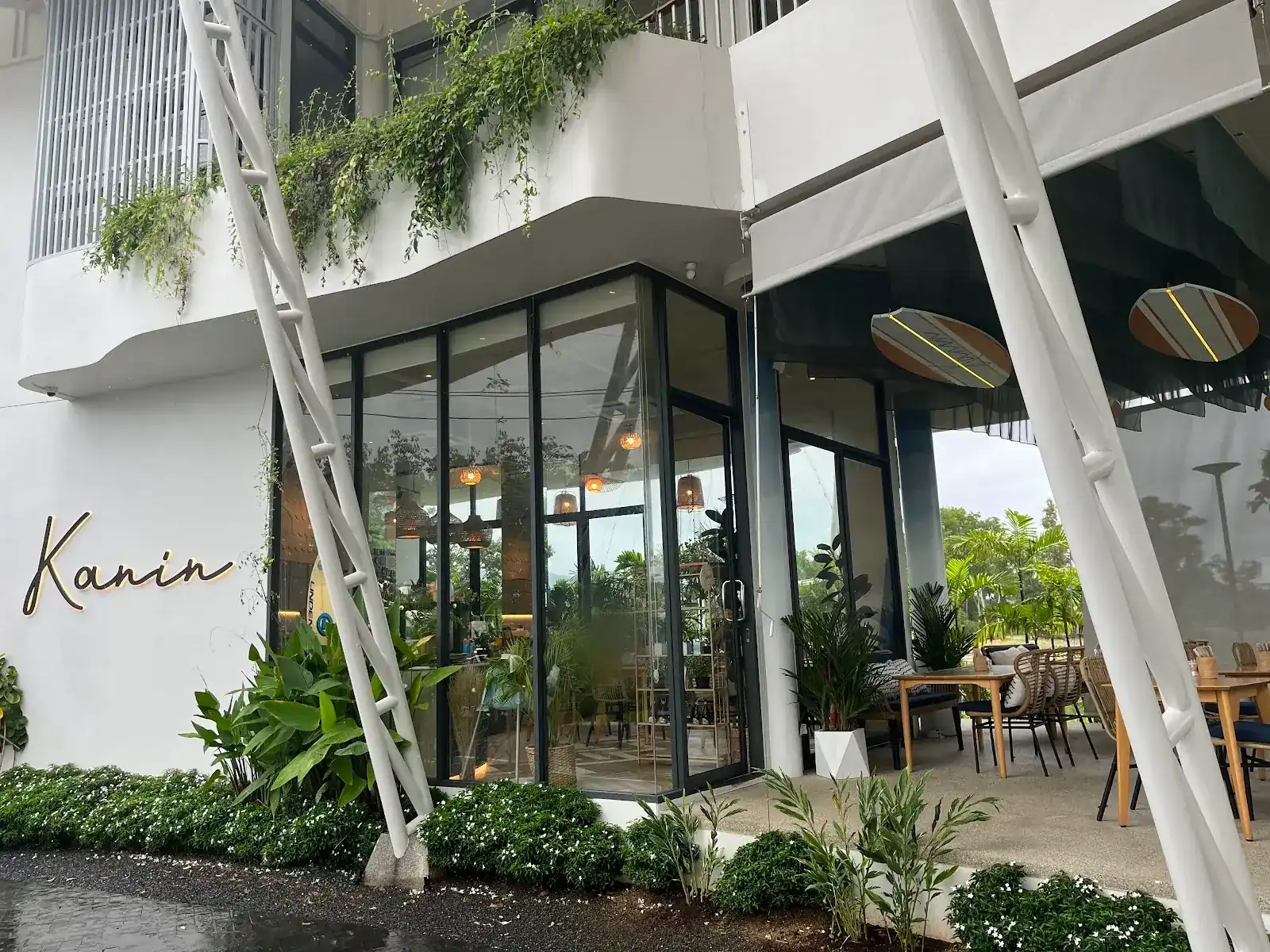 Kanin Café from the street: a white building with plants trailing from the balconies, a glass-walled corner room and tables under the awning