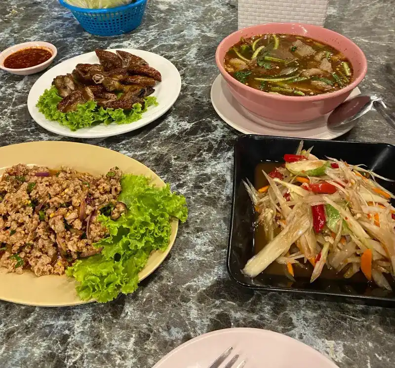 Larb on lettuce, grilled meat, a bowl of spicy soup and papaya salad on one table