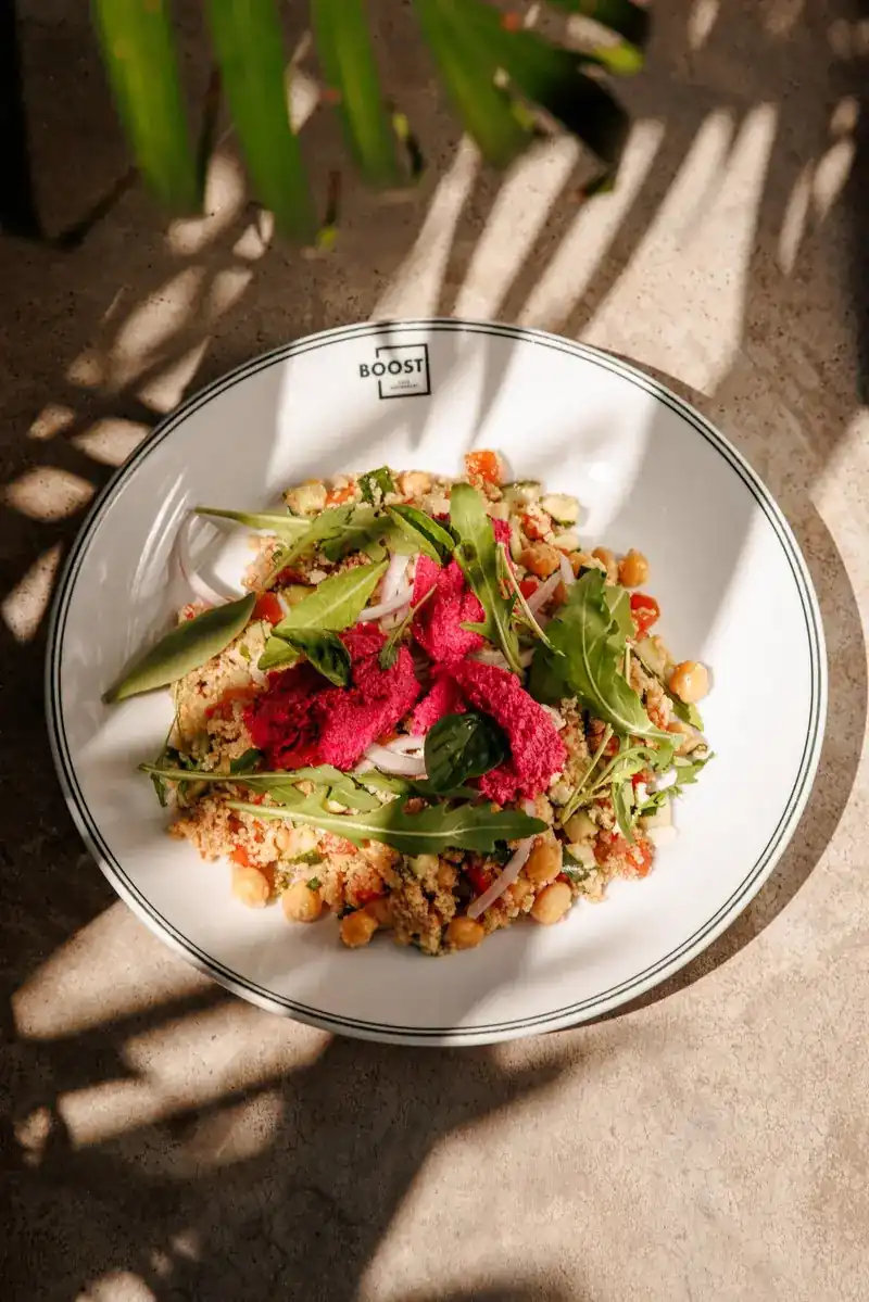 A BOOST plate of couscous, chickpeas and rocket topped with beetroot hummus, in palm-leaf shade