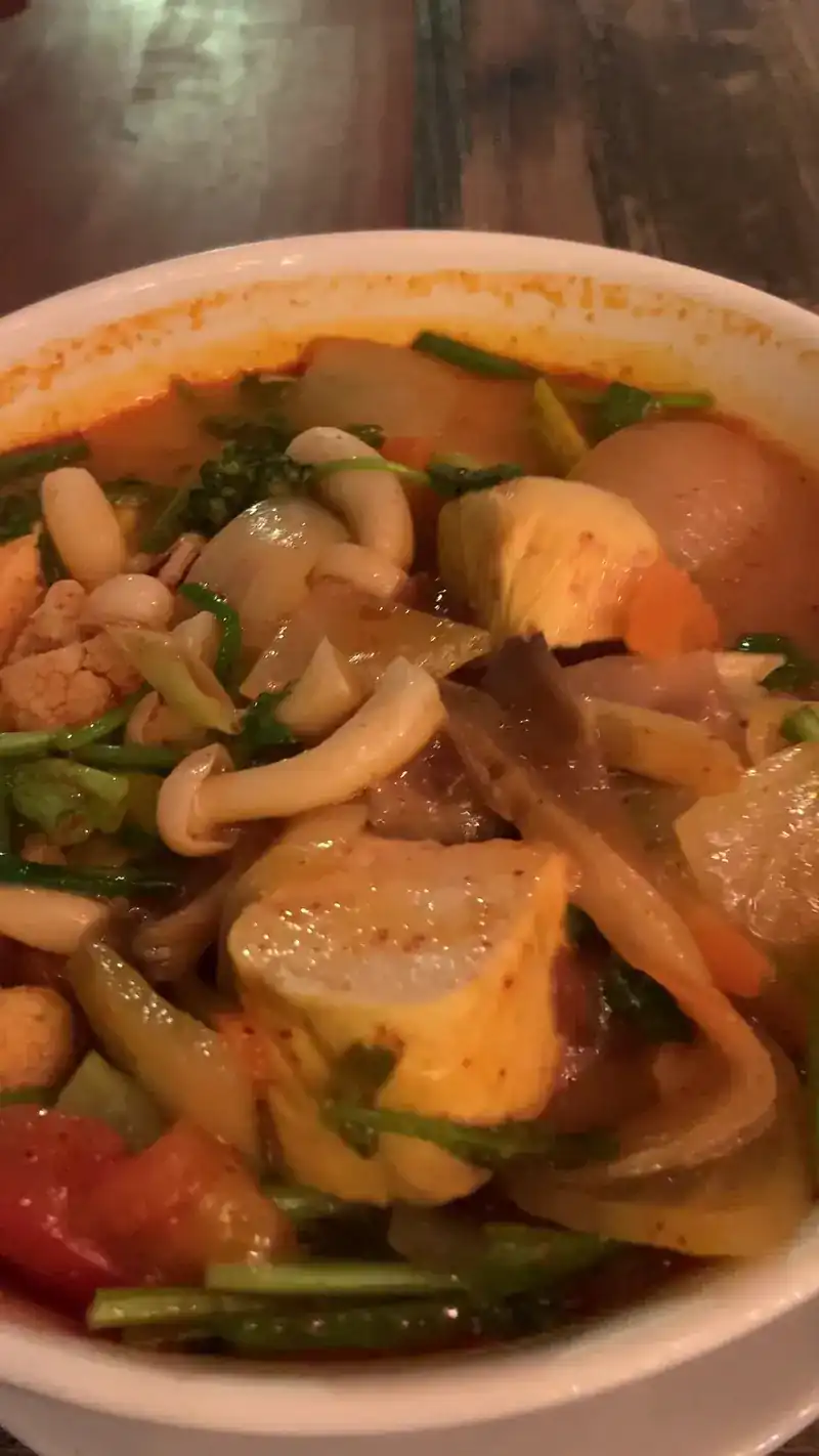 A bowl of soup with tofu, mushrooms, tomato and herbs