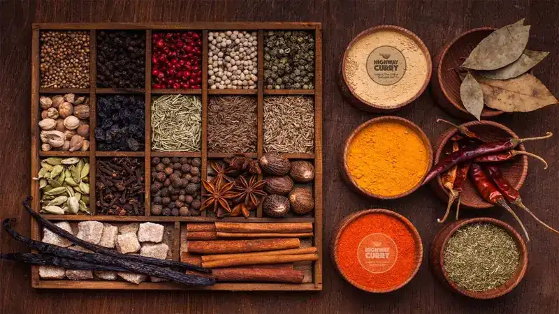 A wooden box of whole spices beside bowls of ground turmeric and chilli