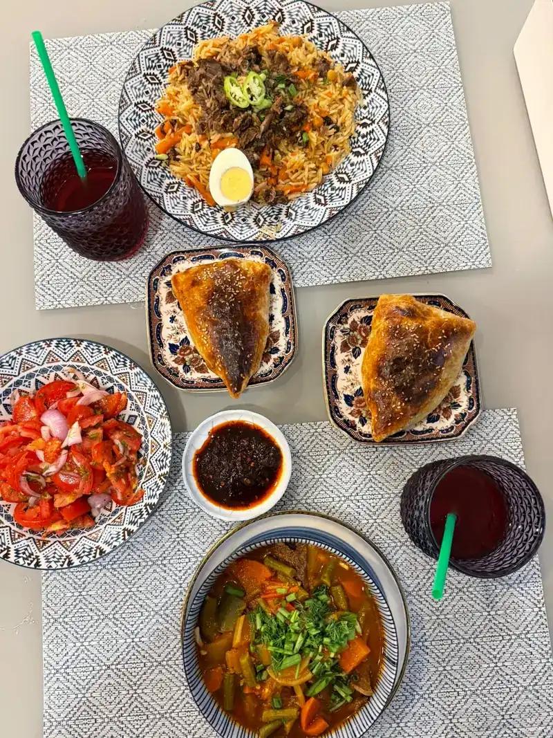 Plov, baked pastries, tomato salad and a bowl of soup on one table