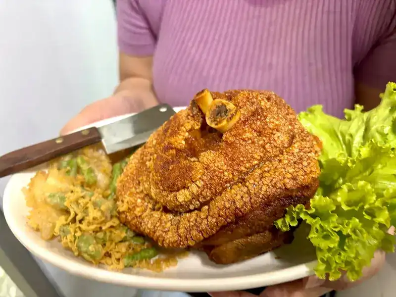 A deep-fried pork knuckle with crackling skin, carried to the table