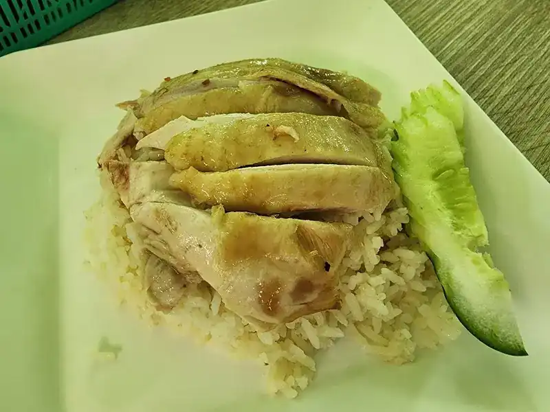 Sliced boiled chicken on rice with a wedge of cucumber