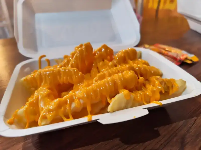 Thick fries under orange cheese sauce in a takeaway box