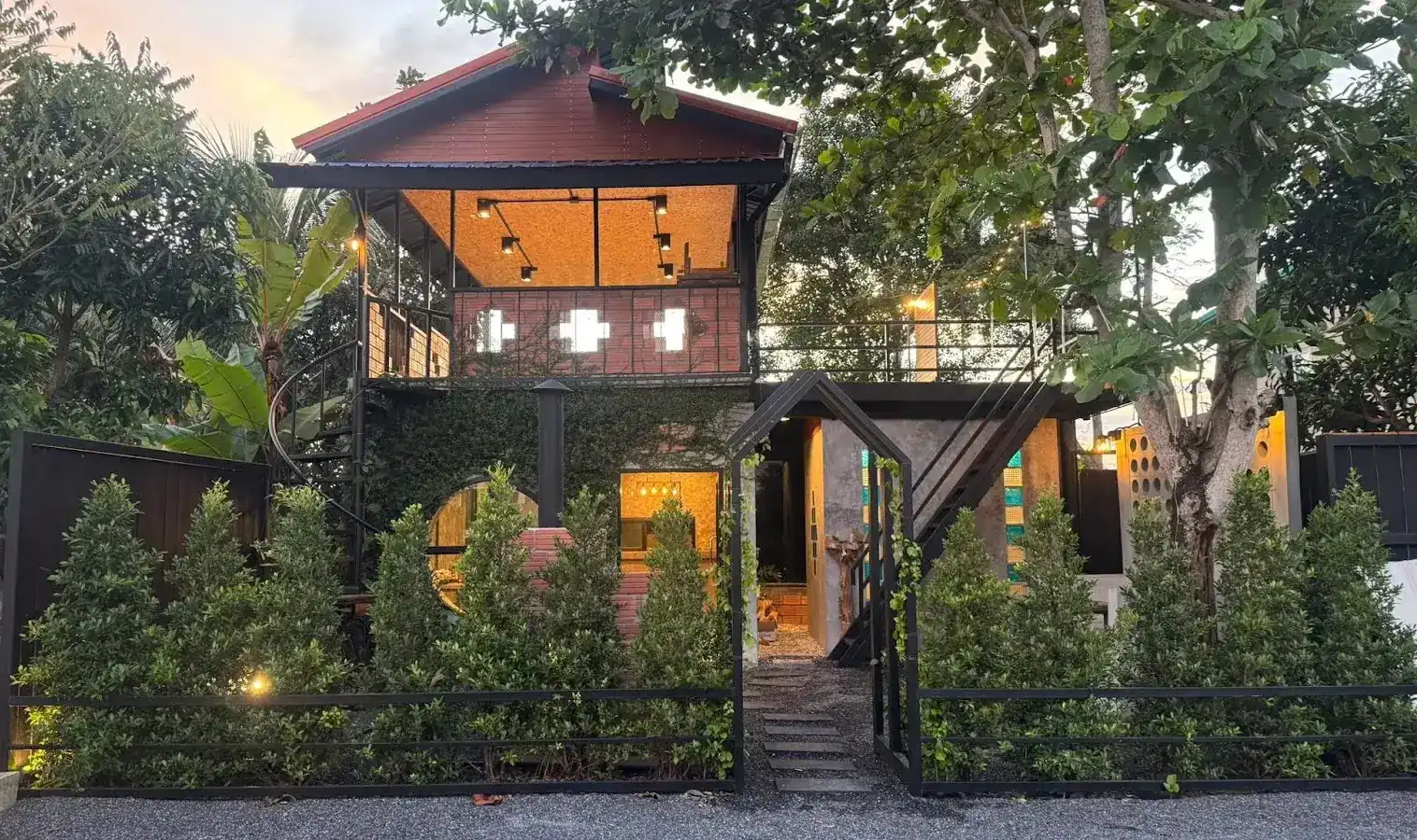 The two-storey wooden house of Khieng Nuea at dusk, lit up behind a clipped hedge