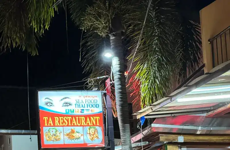 The lit TA RESTAURANT sign, Sea food Thai food, under a palm tree at night / ป้ายไฟ TA RESTAURANT อาหารทะเล อาหารไทย ใต้ต้นปาล์มยามค่ำ