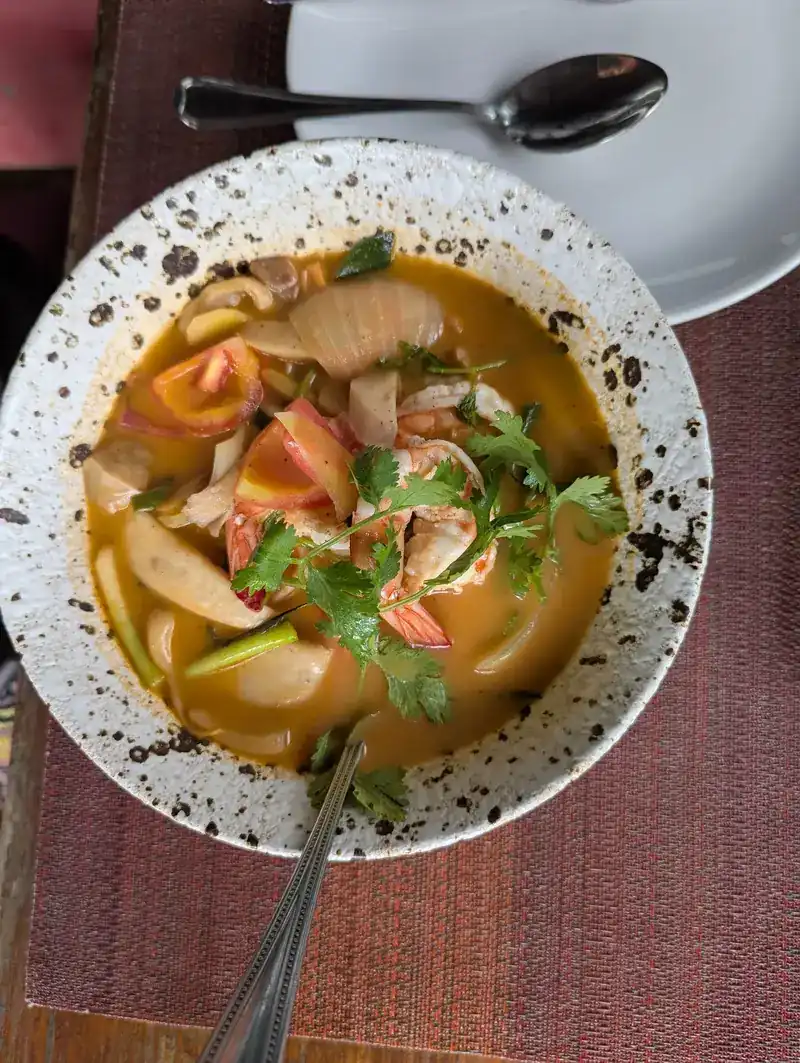 A speckled bowl of tom yum with prawns and herbs