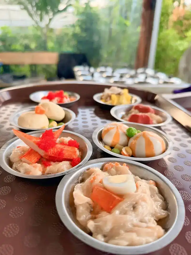 Dim sum in small steel cups: dumplings topped with crab stick and orange roe, steamed buns, and a dumpling with quail egg