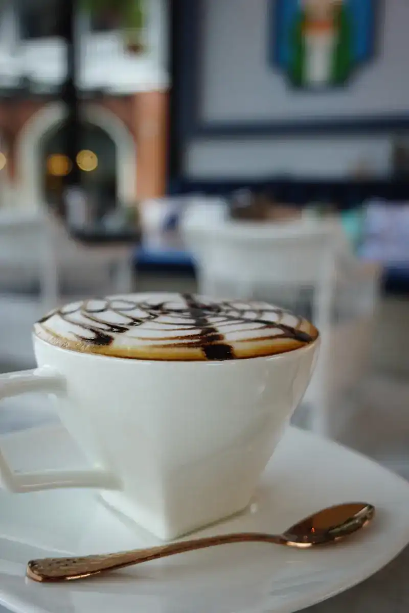 A hot drink with chocolate-drizzled foam and a gold spoon