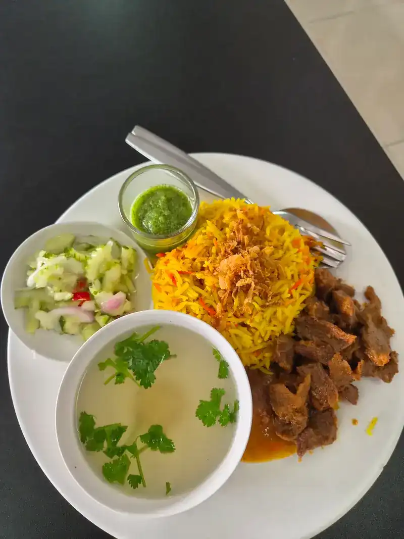 Beef biryani with yellow rice, cucumber relish, green dipping sauce and clear soup