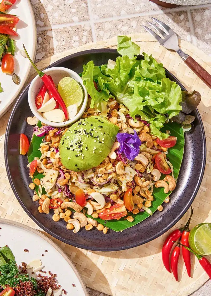 A bowl of shredded vegetables, cashews, avocado and lettuce on a banana leaf