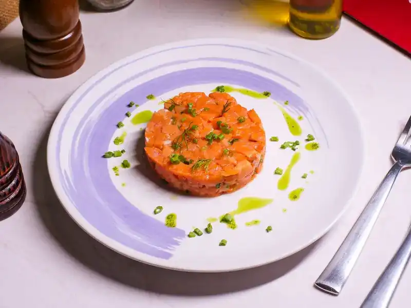 A round of diced salmon with herbs and green oil on a lilac brushed plate