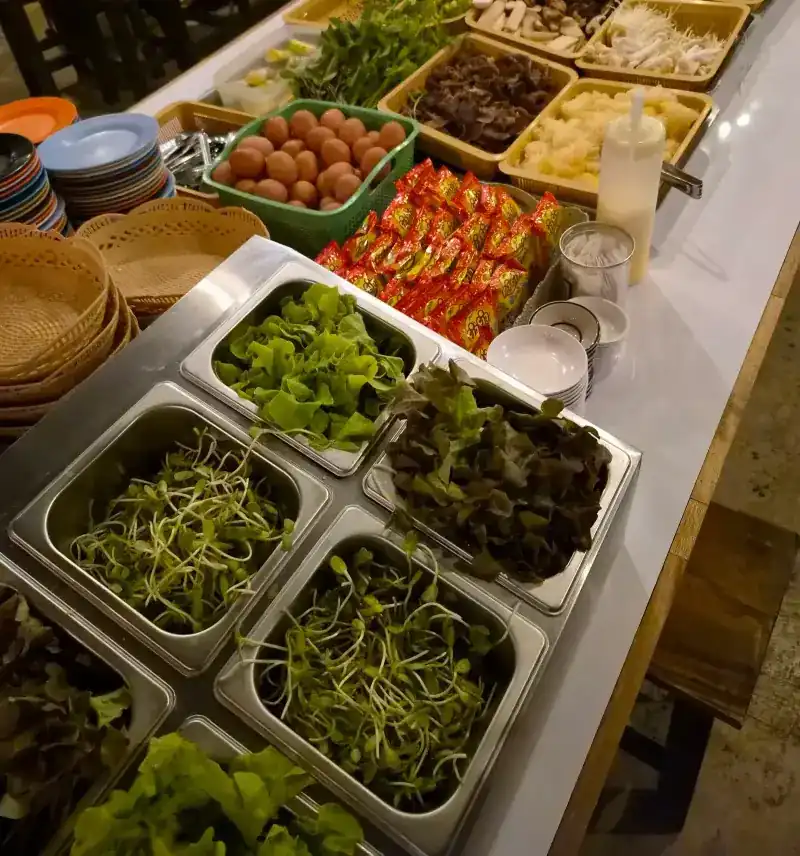 Steel trays of lettuce and shoots on the buffet counter, with eggs, mushrooms and instant noodles behind