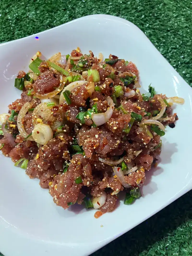 Larb with sliced shallots, spring onion and toasted rice on a white plate