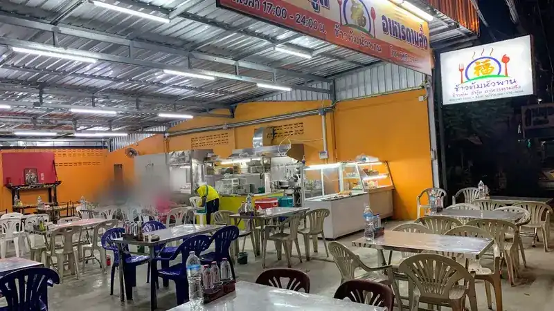 The dining area at night: rows of steel tables and plastic chairs under fluorescent tubes, the kitchen counter and the lit shop sign