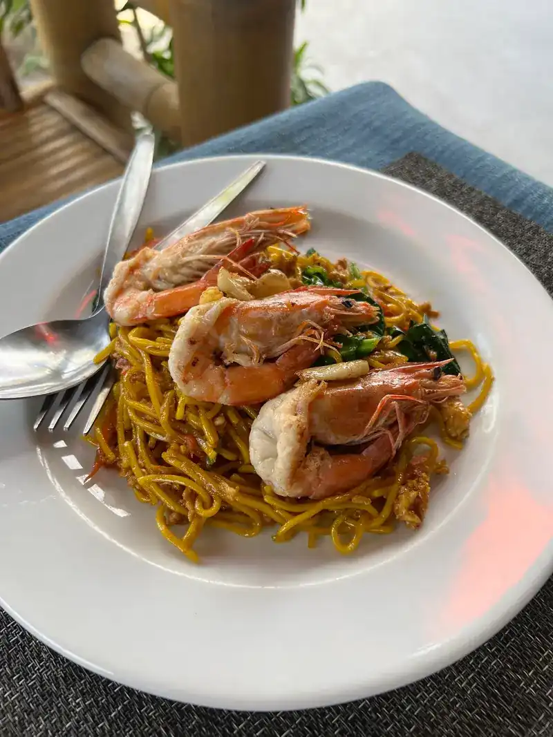 Yellow noodles stir-fried with whole prawns and greens, on a white plate