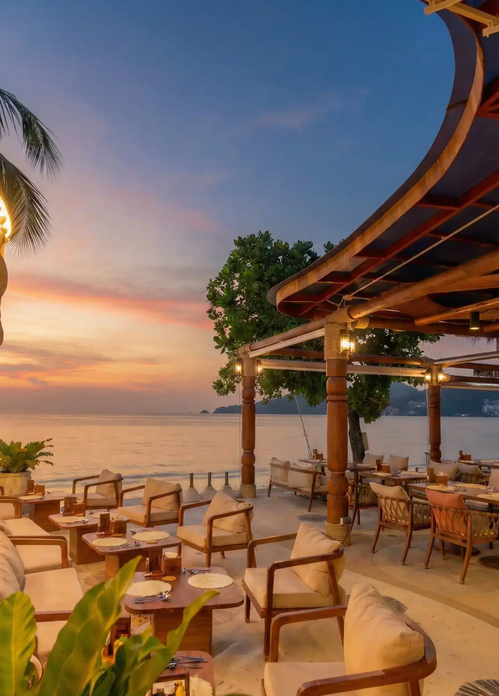 The beach-side terrace of Kan's haus at sunset: wooden armchairs under a timber roof, with Patong Bay behind