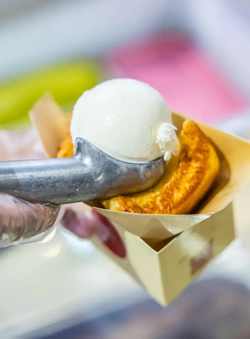 A scoop of white ice cream being set onto a golden grilled bun