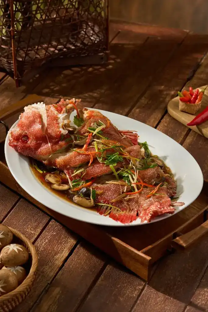 Whole steamed red snapper with ginger, mushrooms and soy on a white platter