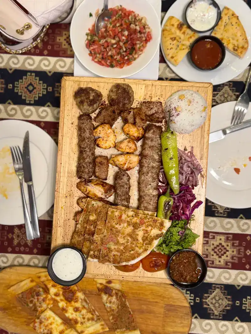 A mixed grill board seen from above: kofte, Adana kebab, chicken, lahmacun, rice and grilled peppers