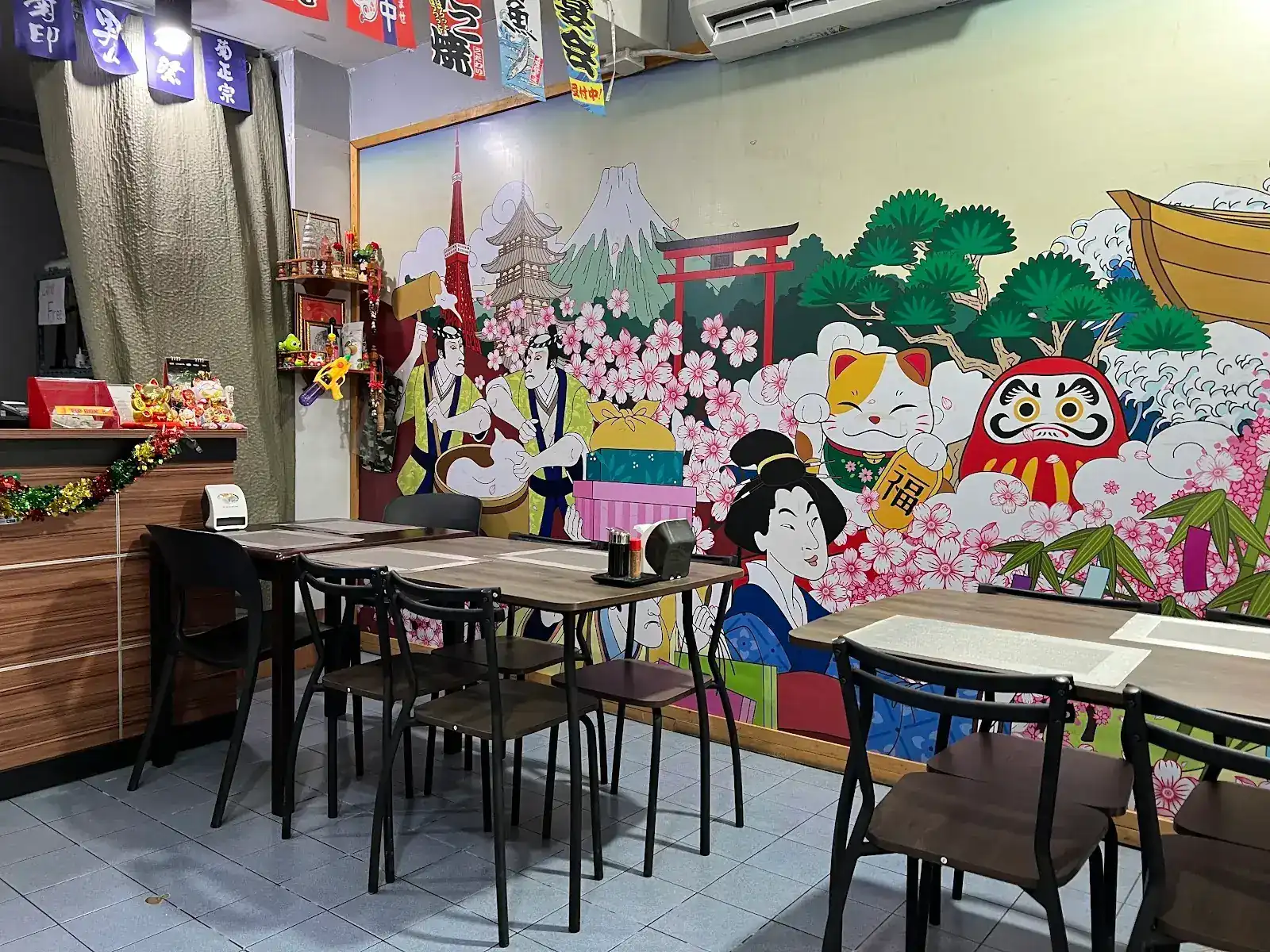 Kin Sushi's dining room: wooden tables in front of a wall painted with Mount Fuji, a red torii gate, cherry blossom, a beckoning cat, a daruma and a geisha