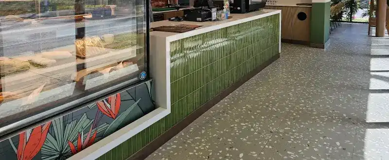 The counter faced with glazed green tiles, a glass display case and the terrazzo floor