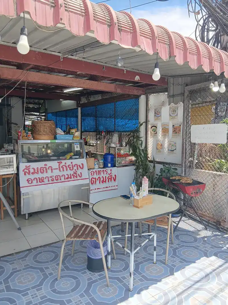 The counter under the awning with its sign for papaya salad, grilled chicken and food to order, a woven basket on top and the grill beside a small table