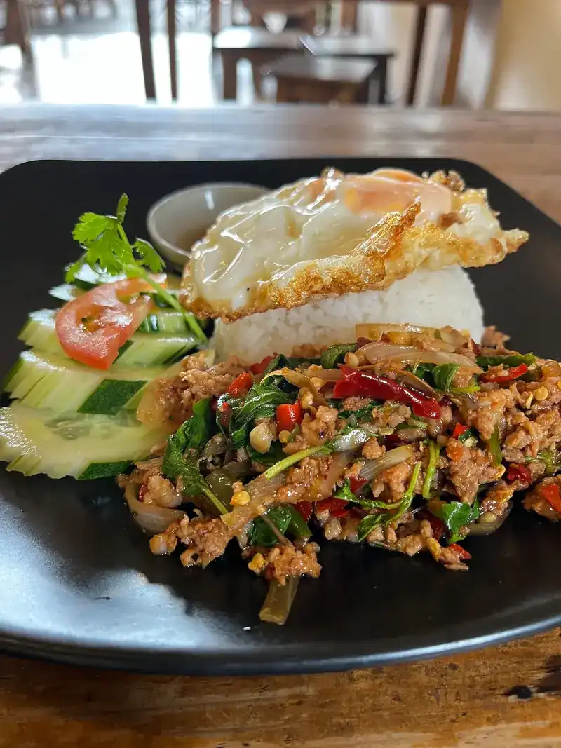 Stir-fried minced pork with holy basil and a fried egg on rice, with cucumber and tomato