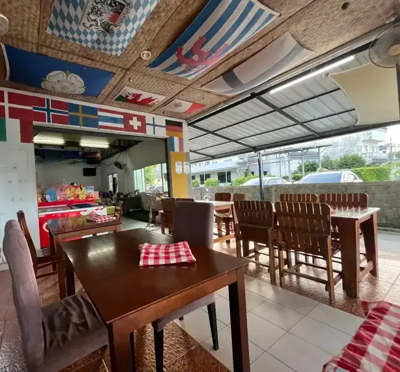 The open-sided dining room: wooden tables, red-check napkins, flags painted over the kitchen door and spread across the woven ceiling