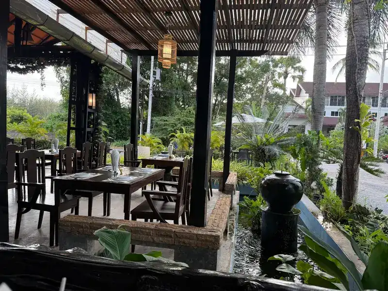 Tables at the garden edge beside a small pond and a dark water jar