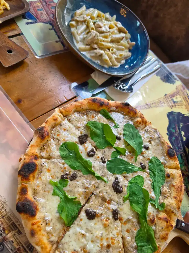 White pizza topped with rocket, with penne in a creamy sauce behind