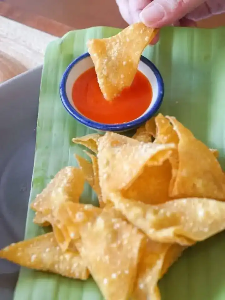 Fried wontons on a banana leaf, one dipped in sauce