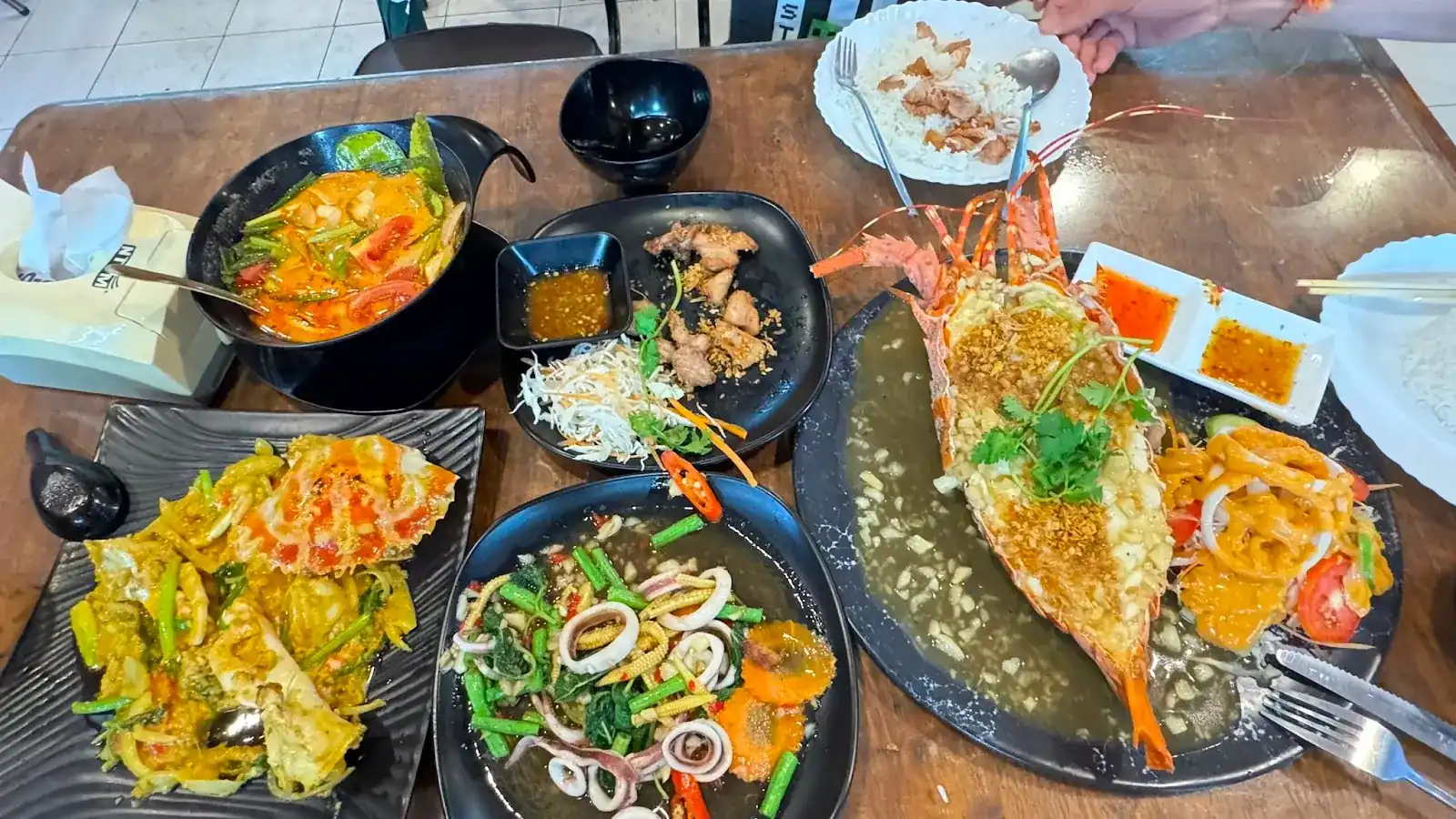 A table of their dishes: a halved lobster under fried garlic, crab stir-fried with curry powder, squid with long beans and a bowl of soup