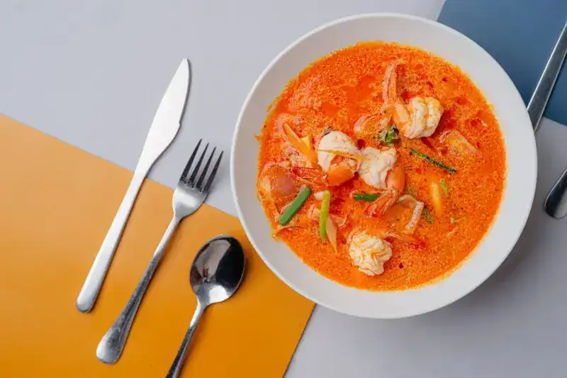 A bowl of orange curry soup with prawns