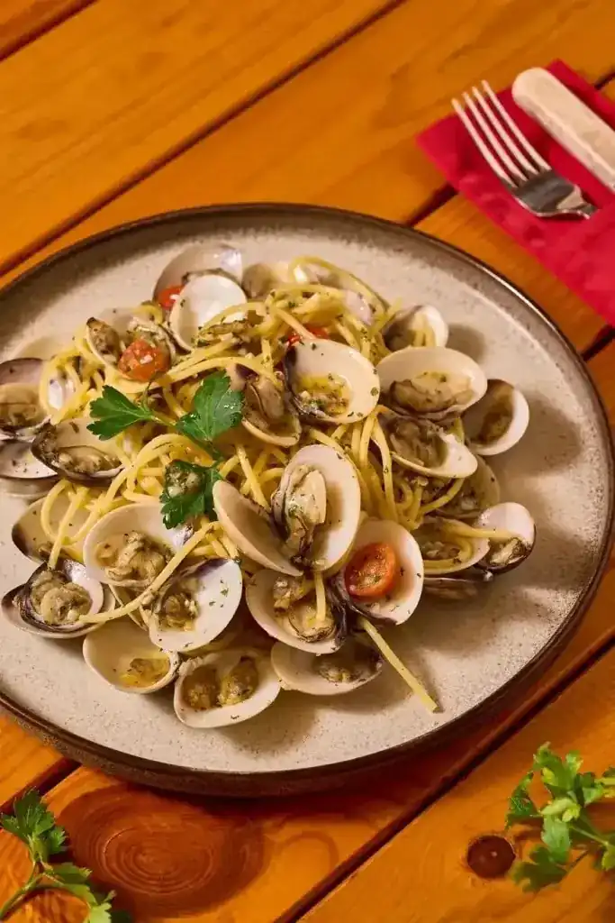 Spaghetti with clams, cherry tomatoes and parsley on a wooden table