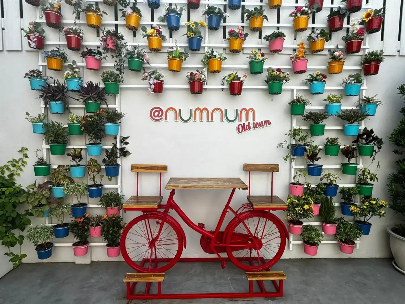 White garden wall covered in colourful flower pots, with the numnum Old Town sign and a red bicycle table
