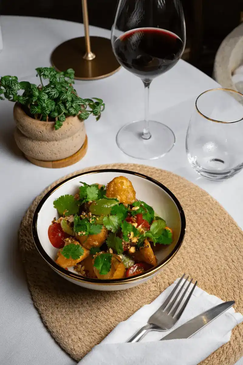 A bowl of crisp fried pieces with tomatoes, grapes, coriander and nuts