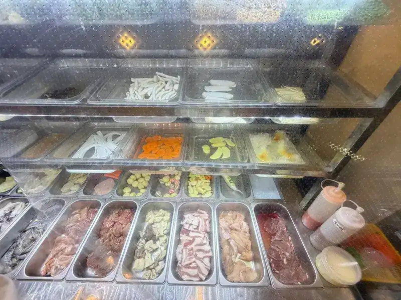 A glass chiller with trays of mushrooms, sliced vegetables, balls, seafood and sliced meats